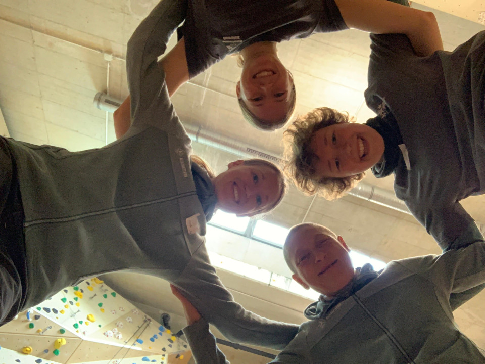 In einer Kletterhalle: Die Kamera liegt am Boden. Vier Frauen bilden einen Kreis indem sie sich an den Schultern festhalten und alle lachen von oben in die Kamera.